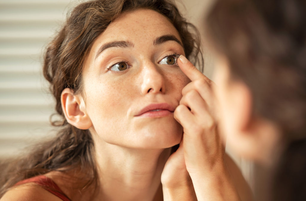 Young woman putting in contact lenses into her left eye. 