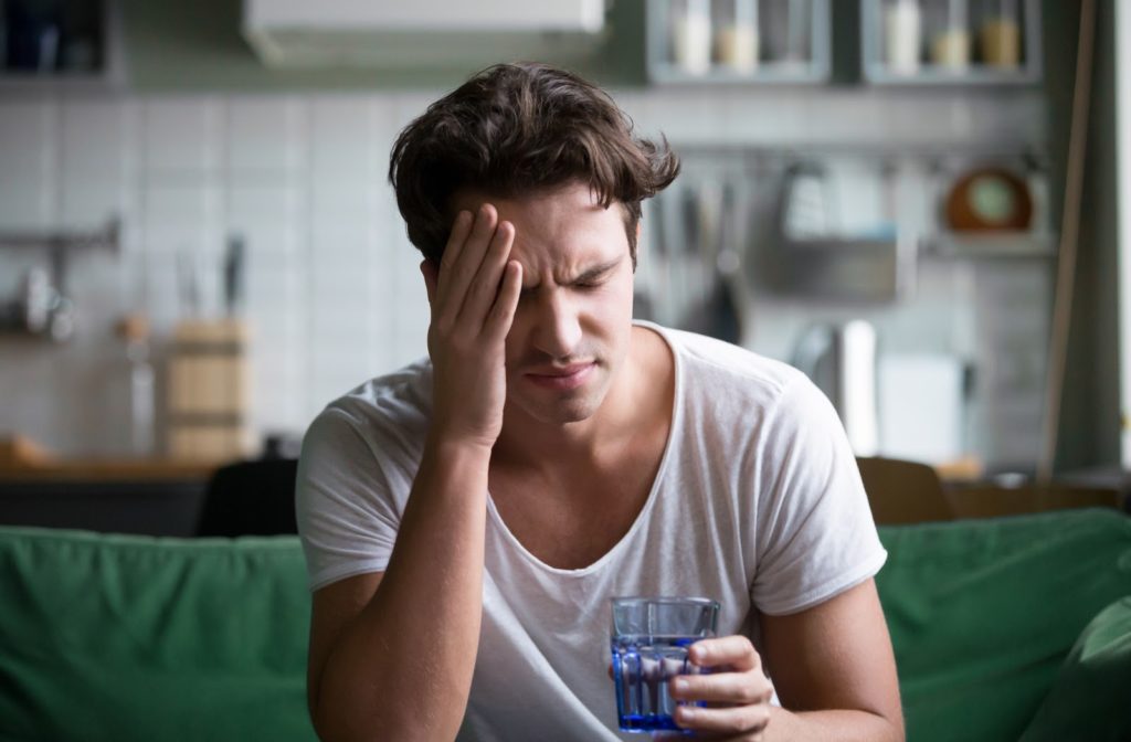 Young man suffering from strong headache sitting with glass of water in the kitchen