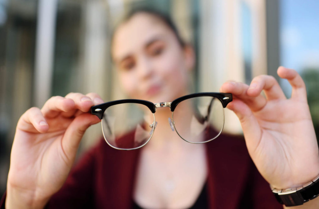 a woman holds up a pair of glasses. the entire image is blurred except for the glasses, which are held closest to the camera