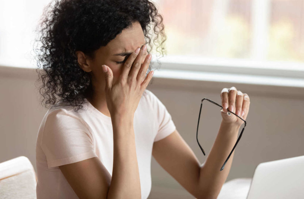 A woman in the office is sitting in front of her computer is rubbing her dry eyes.