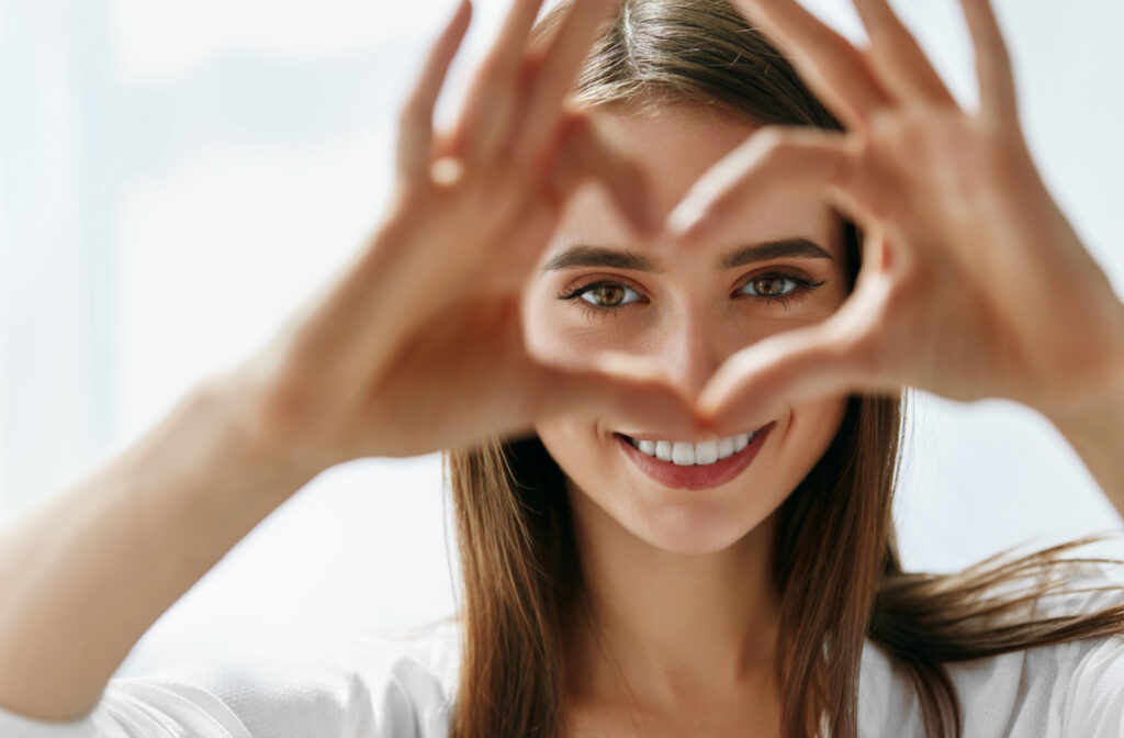 Young woman smiling and holding heart-shaped hands near her eyes