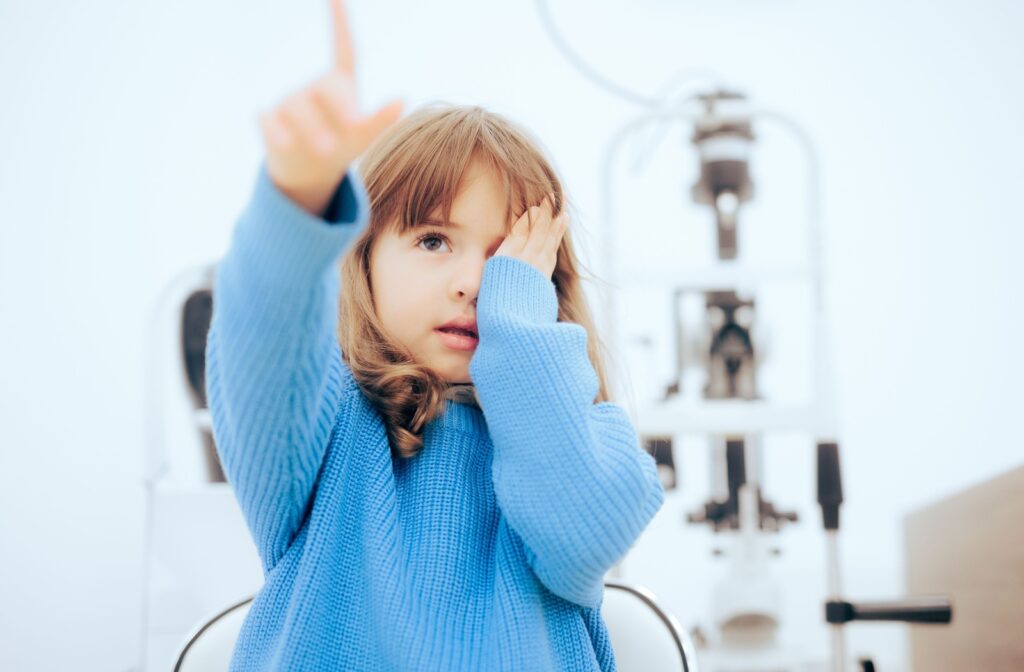 A child covering one eye and pointing with the other during an eye exam to check for myopia.