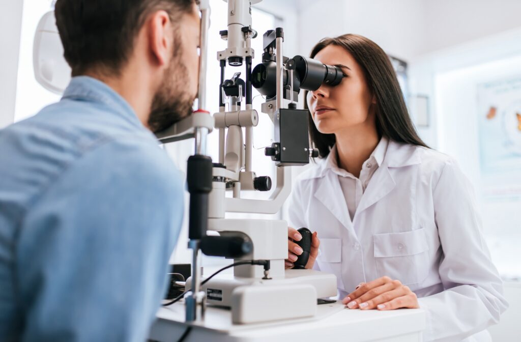 A young female optometrist carefully examining a male patient's eyes during an eye exam.