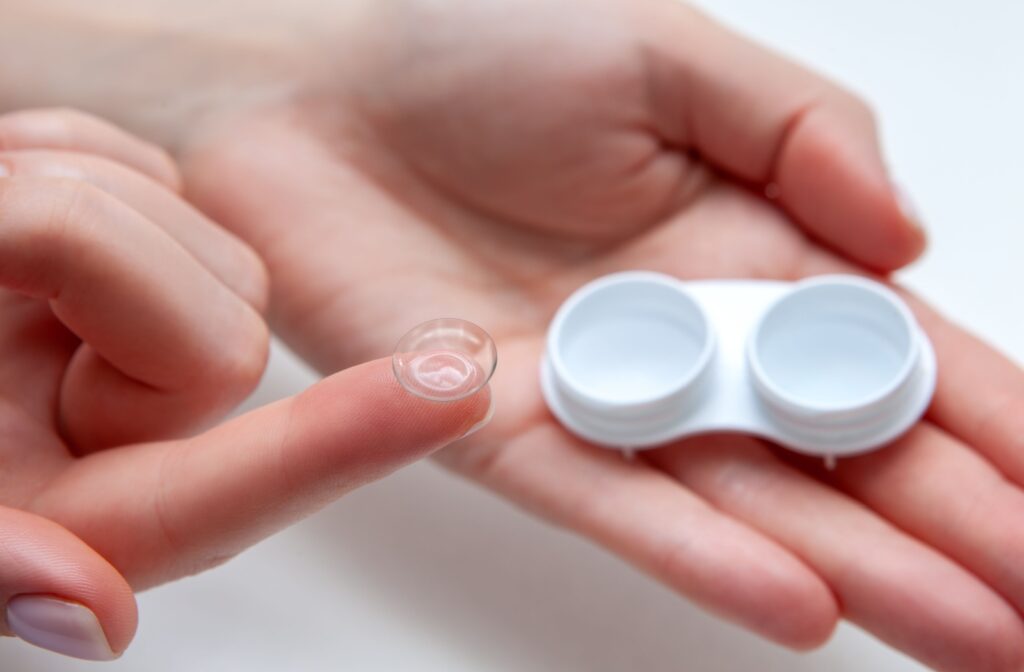 An ortho-k lens on the tip of a woman's finger while a white contact lens case rests in her other hand.