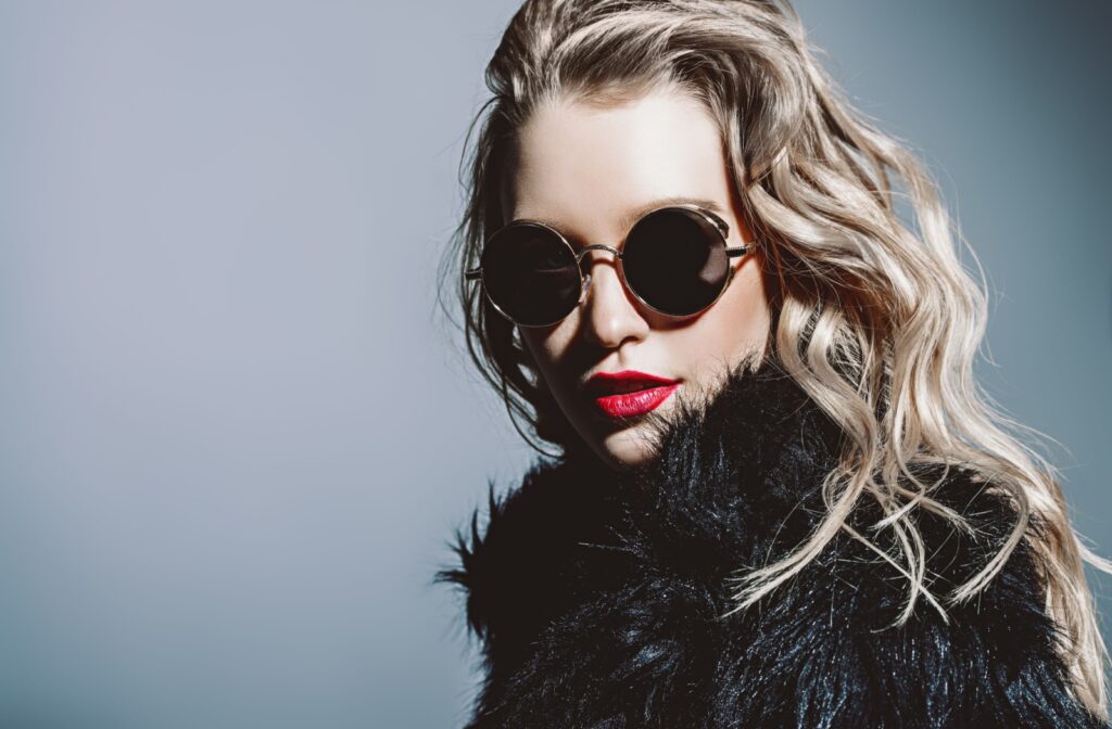 An attractive woman wears sunglasses and a furry winter jacket to protect against winter.