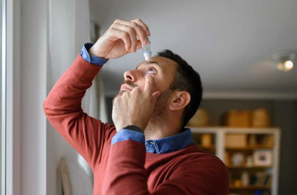 A man is applying eye drops, looking up while using the drops in his eyes for relief from dryness.