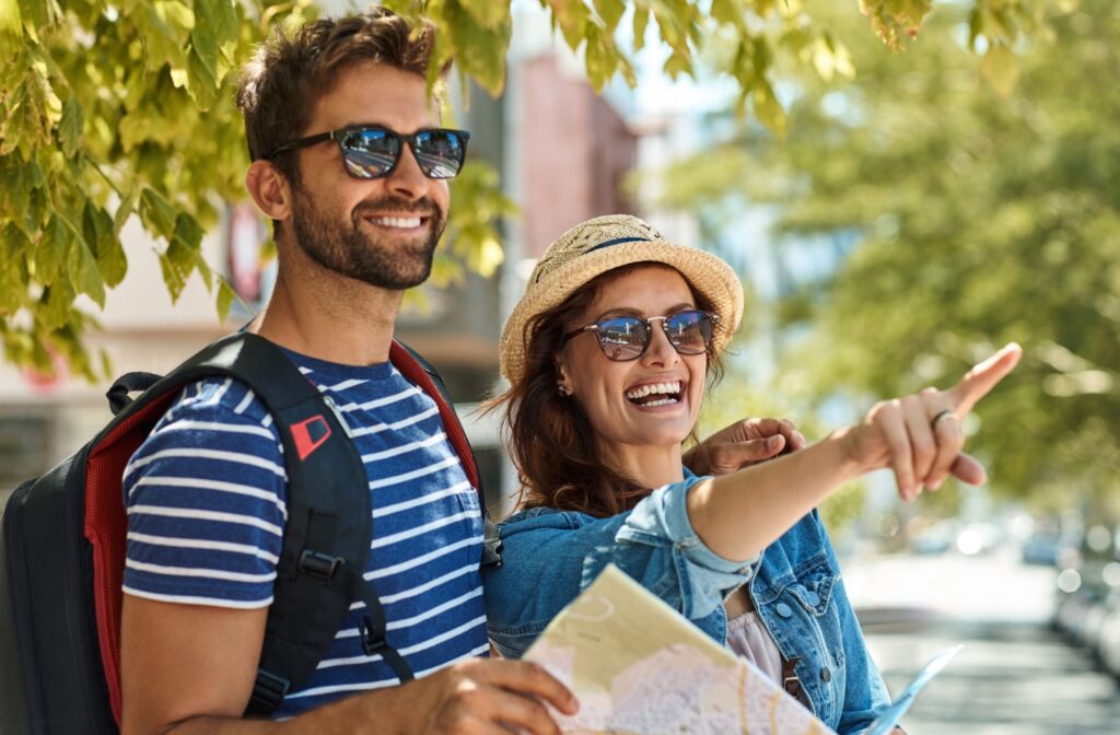 Smiling couple wearing sunglasses and holding a map outdoors.