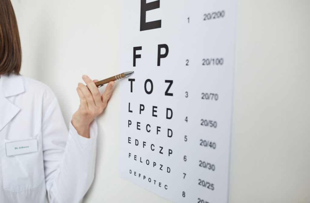 A person in a lab coat points to letters on a Snellen eye chart with a pen.