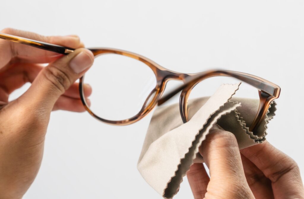 A close-up photo of someone cleaning their glasses lens with a microfibre cloth.