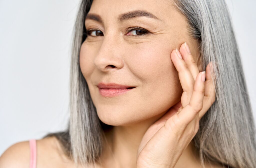 Smiling woman with grey hair gently touching the skin near her eye.