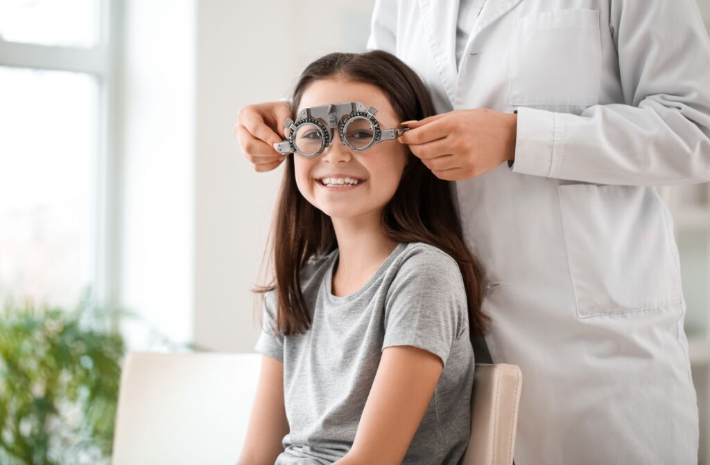 A child smiling while an optometrist adjusts a trial frame on her face during an eye exam.