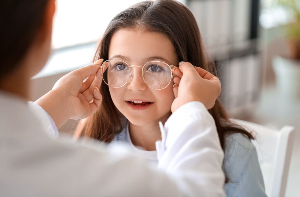 A child trying on a pair of eyeglasses while an optometrist helps adjust the frames.