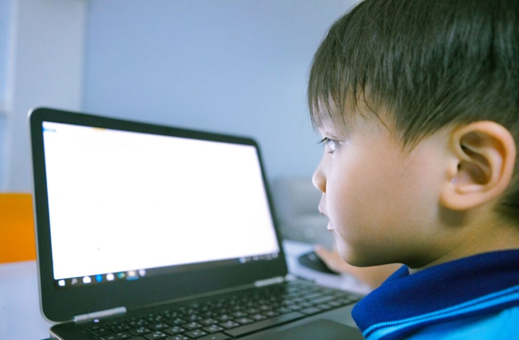 A child closely looks at a laptop screen while sitting indoors, focusing intently on the display.