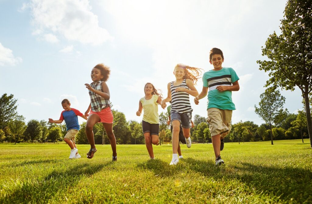 A group of children run and smile while playing outside on a sunny day in a grassy park.