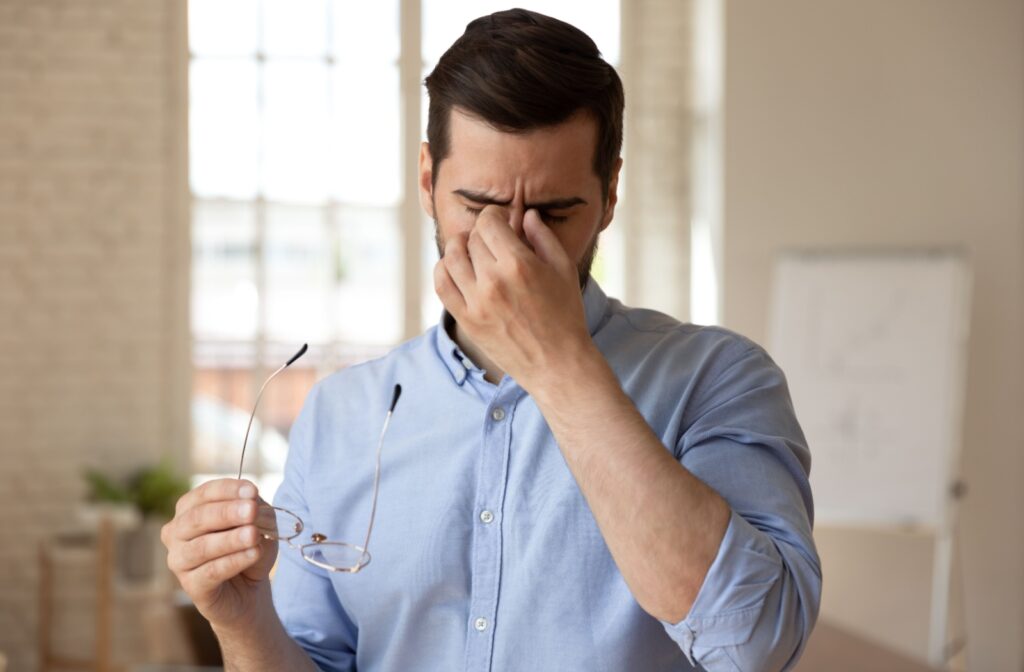 A person rubbing the bridge of their nose between their eyes in discomfort, their other hand holding a pair of glasses.