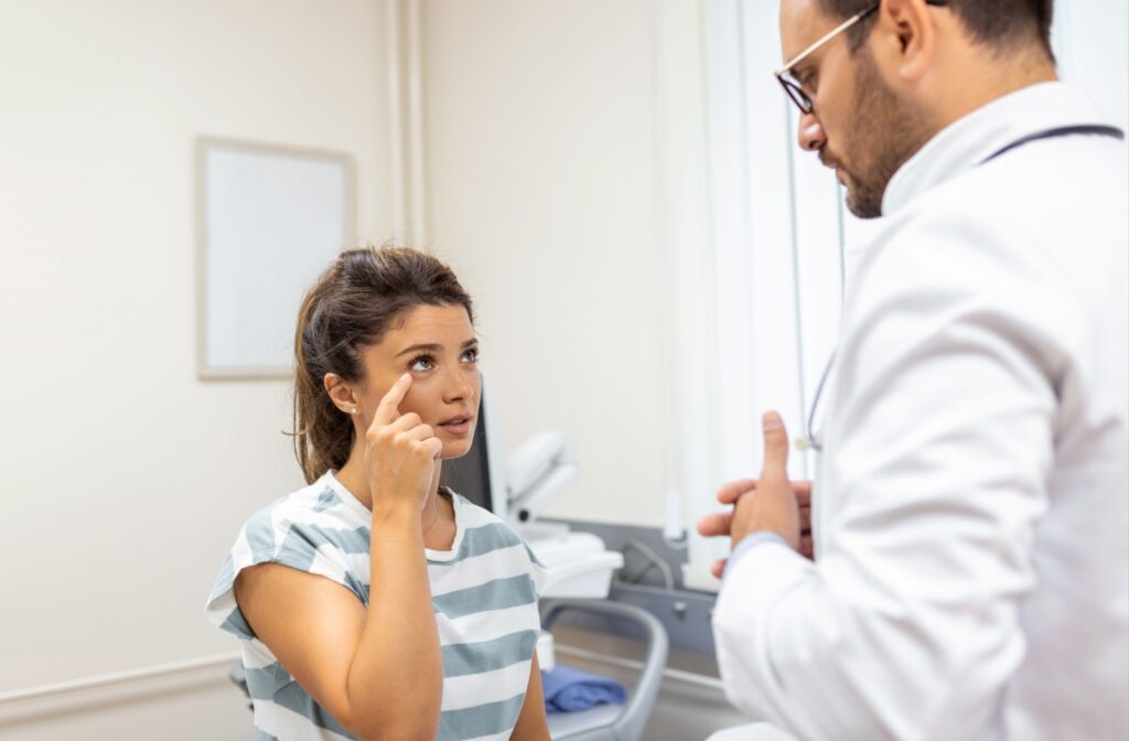 A person sits at the eye doctors office and points to her eye while wearing a striped shirt.