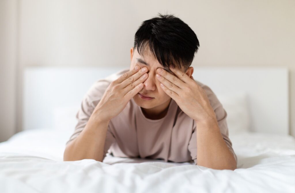 A person lays on a bed and rubs their dry eyes