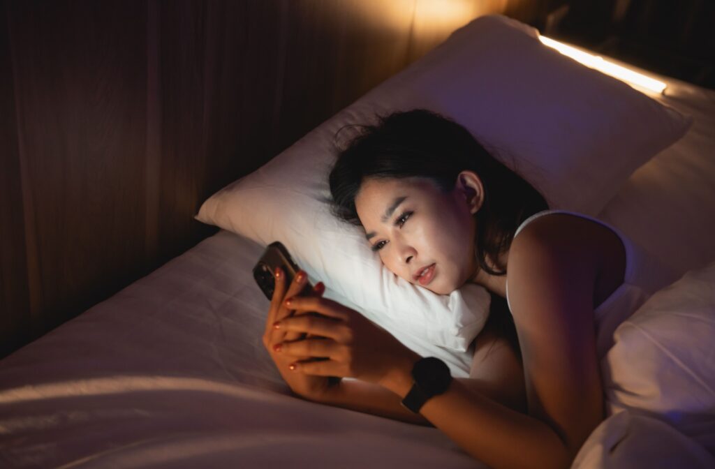 A person lays in bed in a dark room and uses their phone