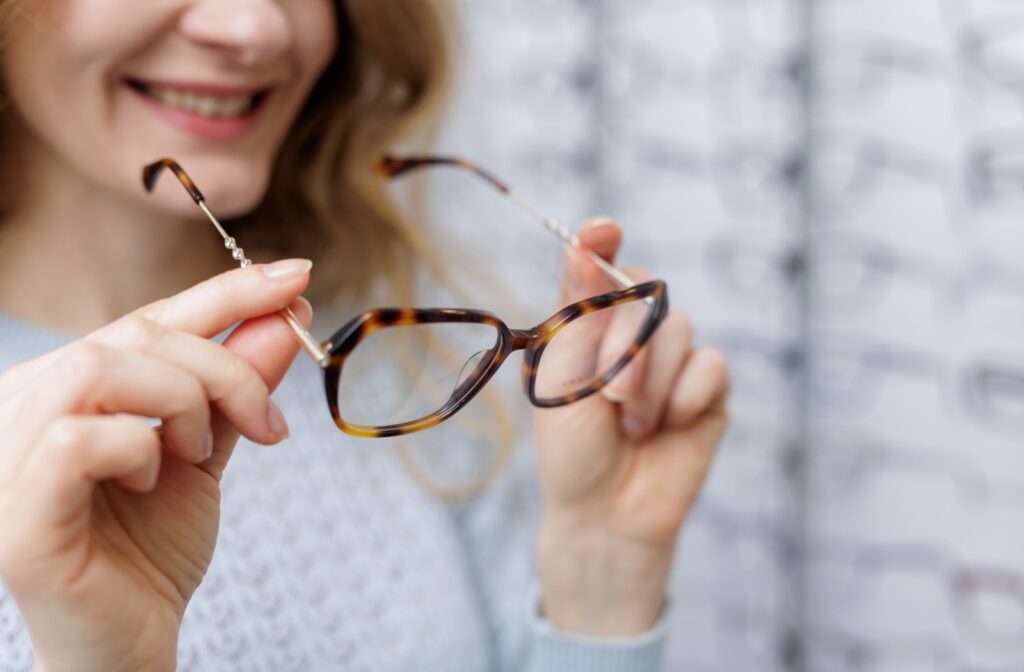 A person smiling while holding a pair of oversized turtle shell glasses